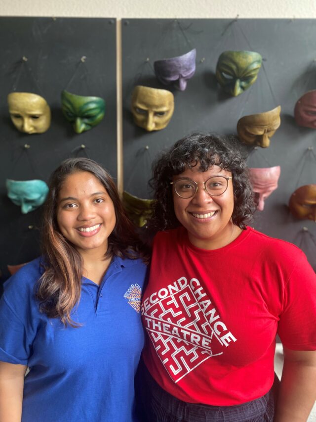 Iman and Nawaal from Second Chance Theatre standing in front of the wall of masks at Geese offices