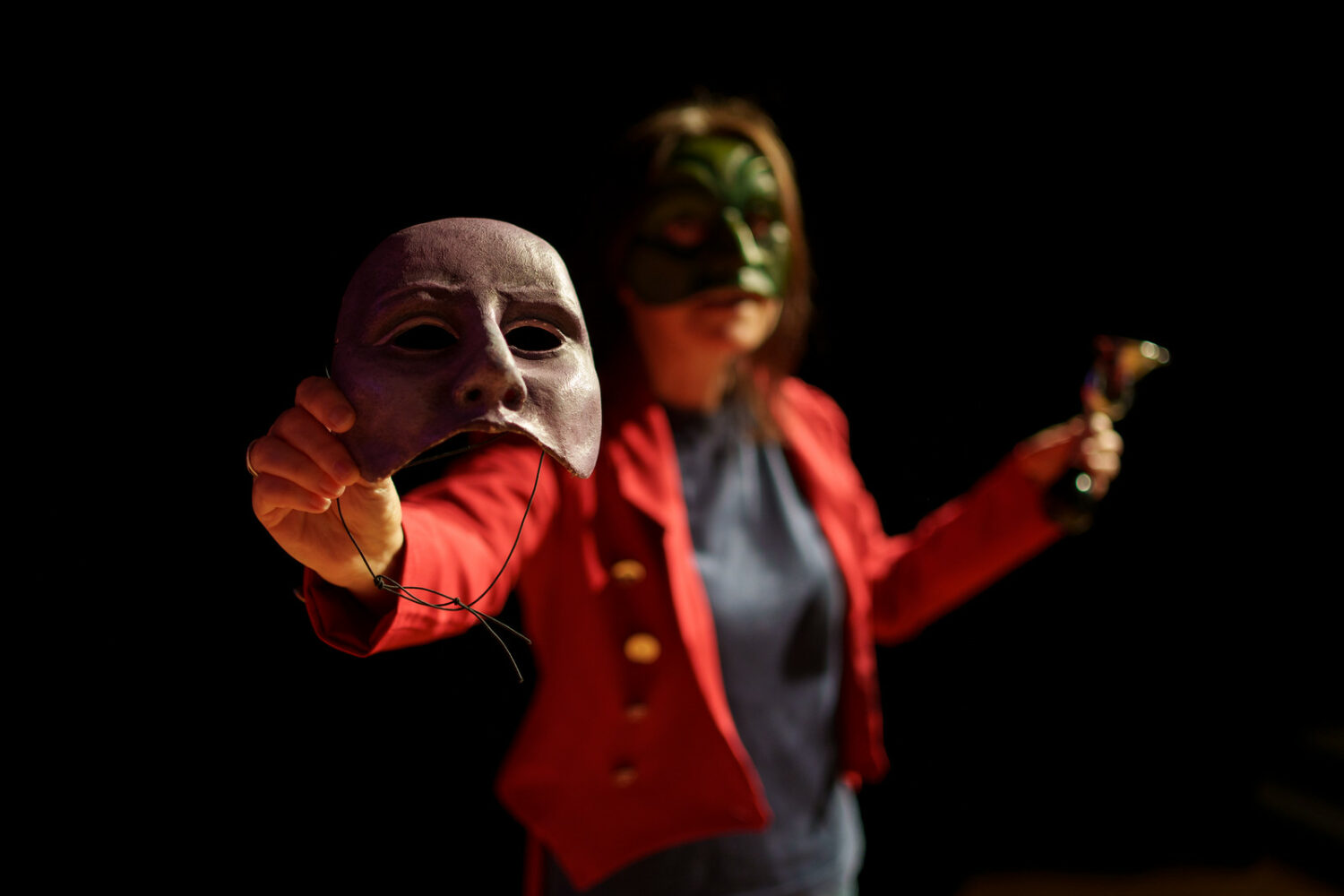 The fool raises a half mask to the camera