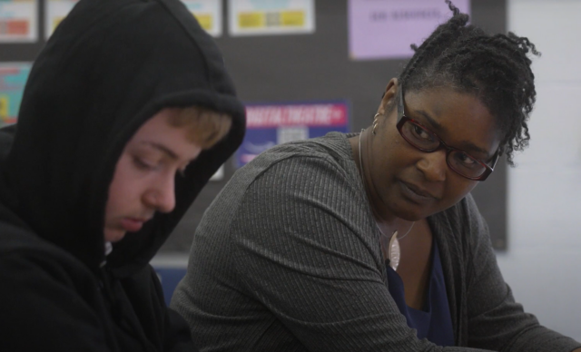 Senior Practitioner, Liz, portrays the Class Teacher in this image. She talks to Ethan, her student, who is wearing his hood up.